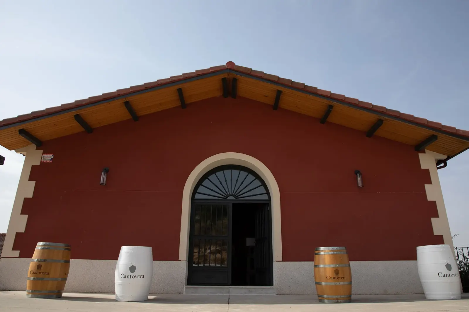 Fachada roja de la bodega con barricas en la entrada